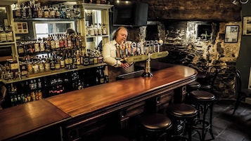 Un bar con mostrador de madera, varias botellas de licor y un bartender.