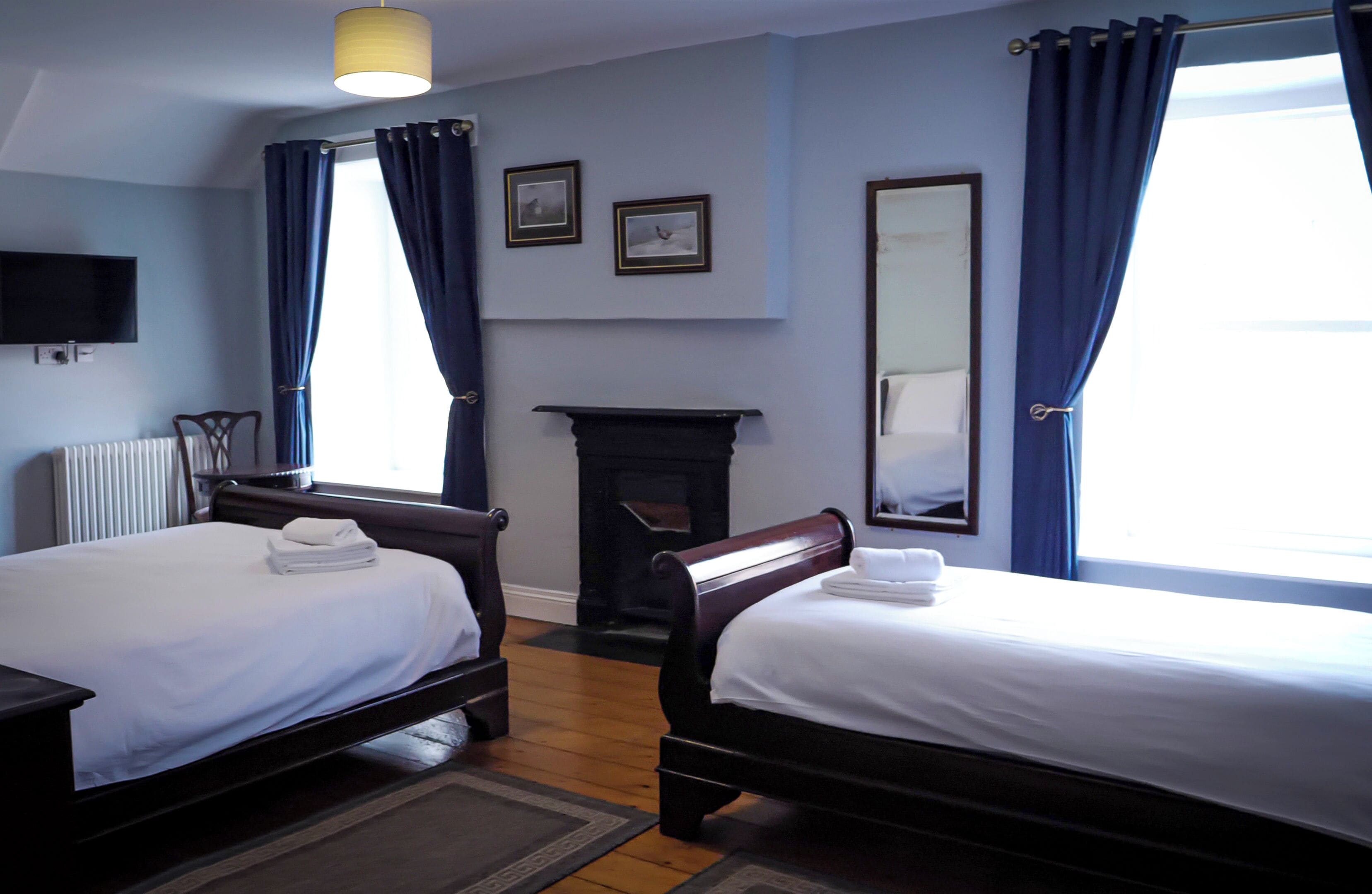 Habitación de hotel con dos camas, chimenea, televisor y un ventanal grande con cortinas.