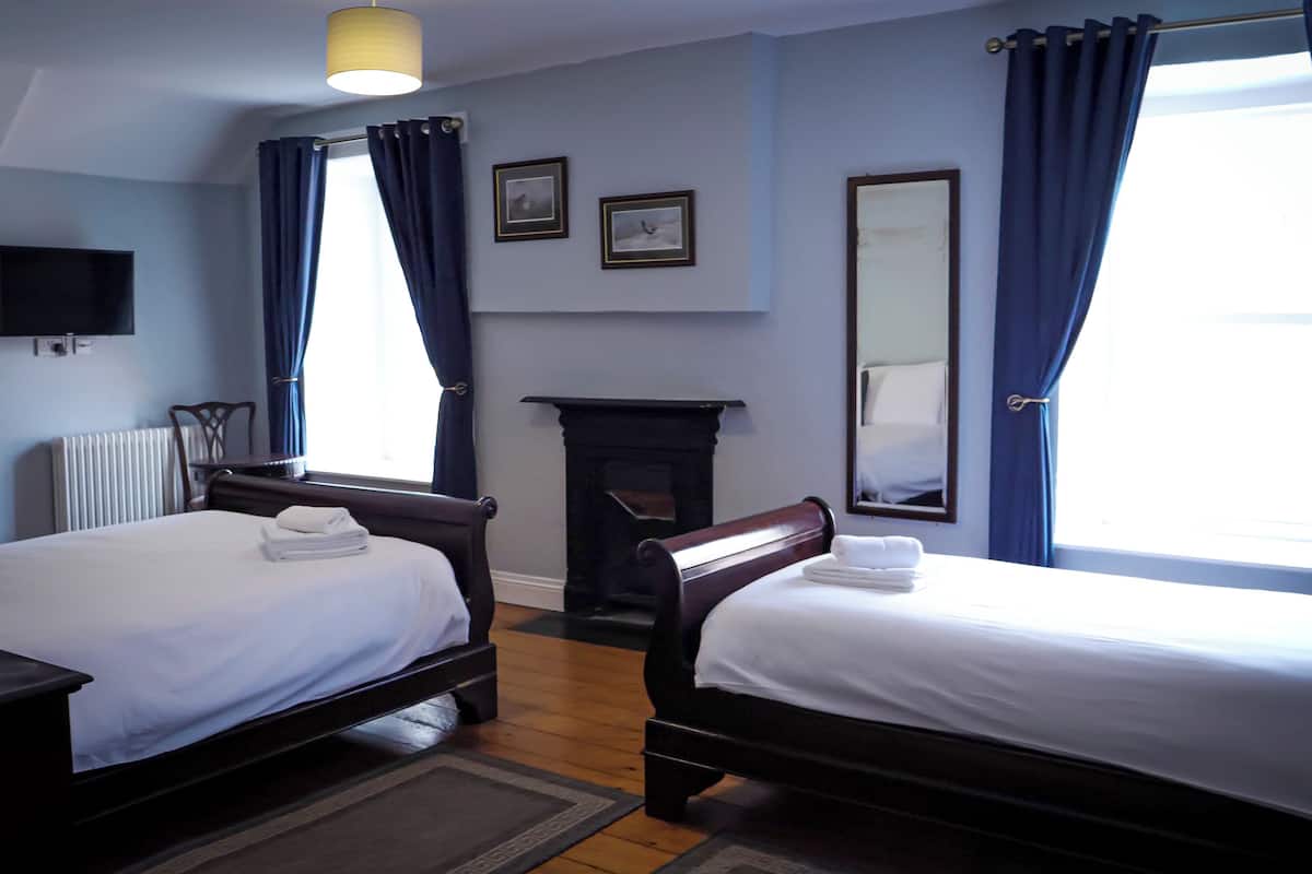 A hotel room with two beds, a fireplace, a television, and a large window with curtains.