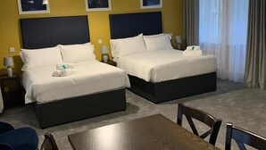 Habitación de hotel con dos camas, una mesa de comedor y vistas al exterior.