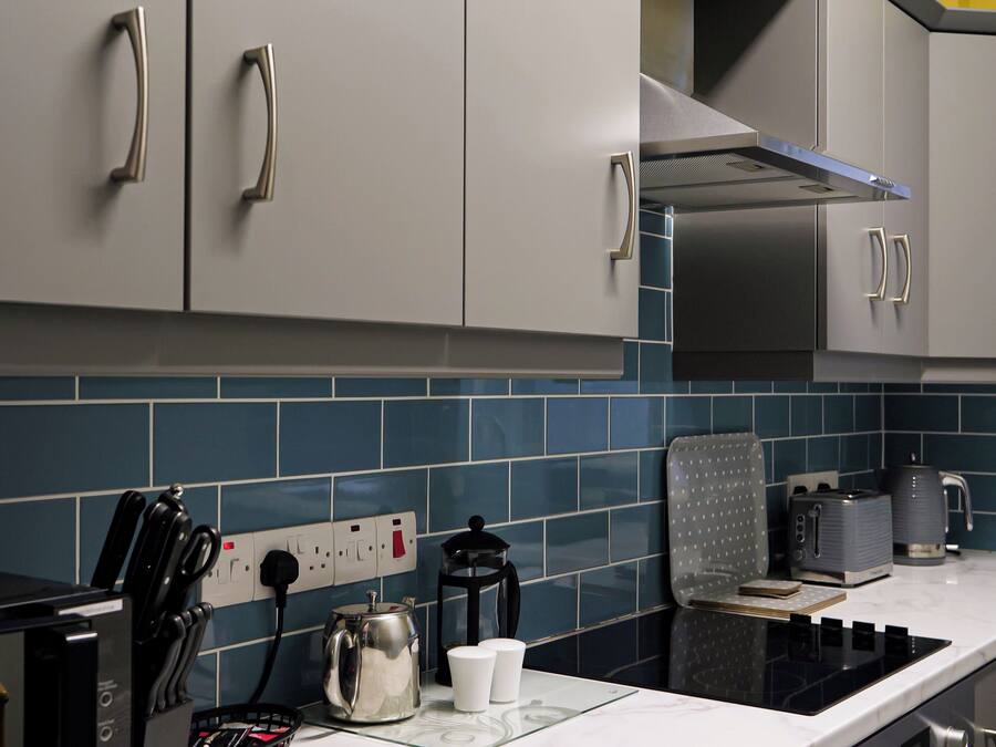 A modern kitchen with grey cabinets, a black countertop, and blue-tiled backsplash.