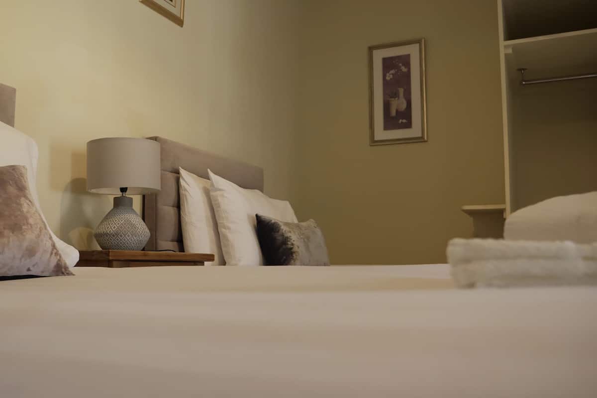 A neatly made bed with a headboard, a bedside lamp, and a framed picture on the wall.