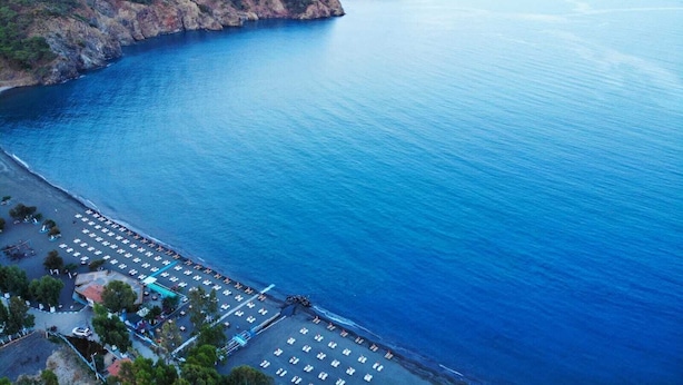 A coastal hotel with a parking lot, beach area, and mountainous backdrop. - Bucak Apart Hotel Göcek (Fethiye)