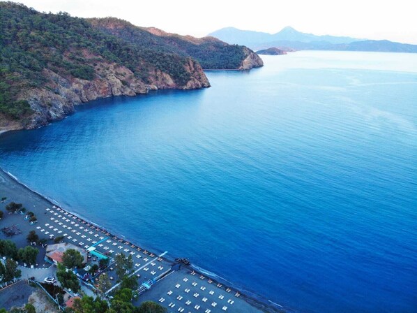 A coastal hotel with a parking lot, beach area, and mountainous backdrop. - Bucak Apart Hotel Göcek - (Beach 1km)  (Fethiye)