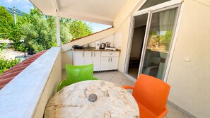 A balcony with a table and chairs, a sliding glass door, and a kitchen area with cabinets and appliances. - Bucak Apart Hotel Göcek (Fethiye)
