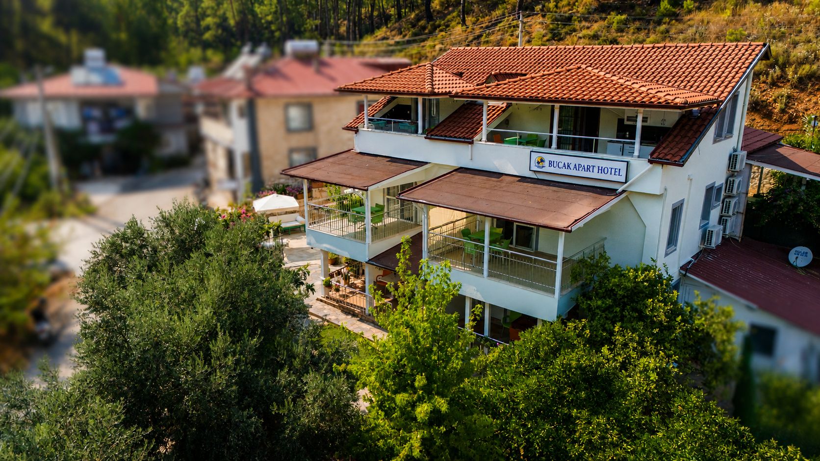 A two-story hotel with a balcony on the upper floor, surrounded by greenery.