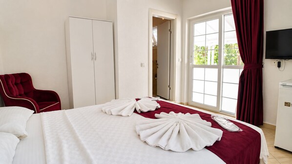 A hotel room with a bed, a red chair, a wardrobe, a television, and a window with curtains.