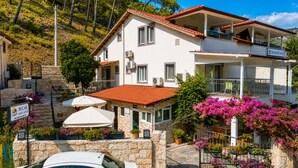 A two-story hotel with a stone facade, multiple balconies, and outdoor seating with umbrellas. - Bucak Apart Hotel Göcek (Fethiye)
