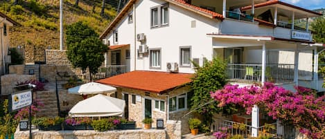 A two-story hotel with a stone facade, multiple air conditioning units, and outdoor umbrellas.