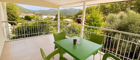 A balcony with a table and chairs, a railing, and a view of greenery and buildings.