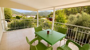 A balcony with a table and chairs, a railing, and a view of greenery and buildings.