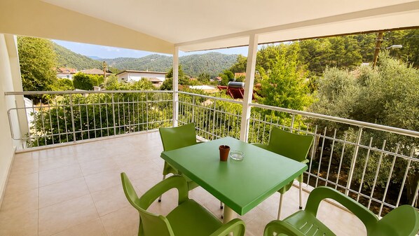 A balcony with a table and chairs, a railing, and a view of greenery and buildings.