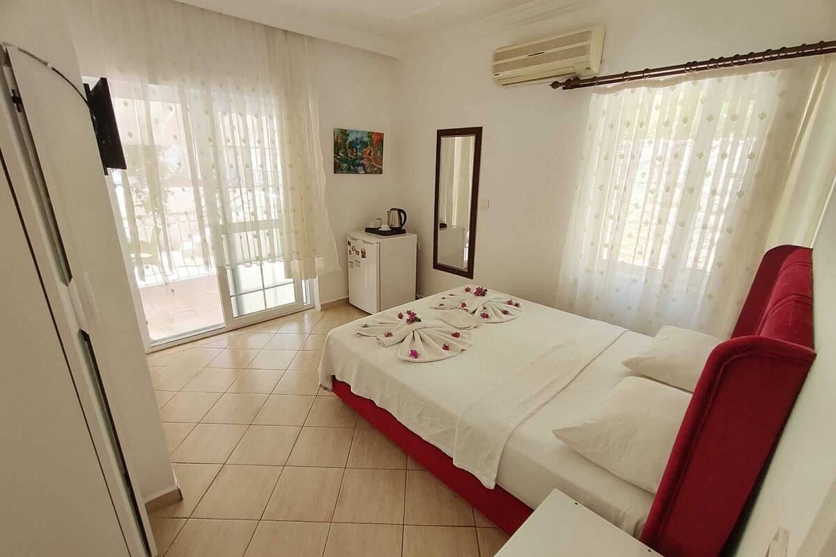 A hotel room with a bed, a small desk, a mirror, and a window with curtains.