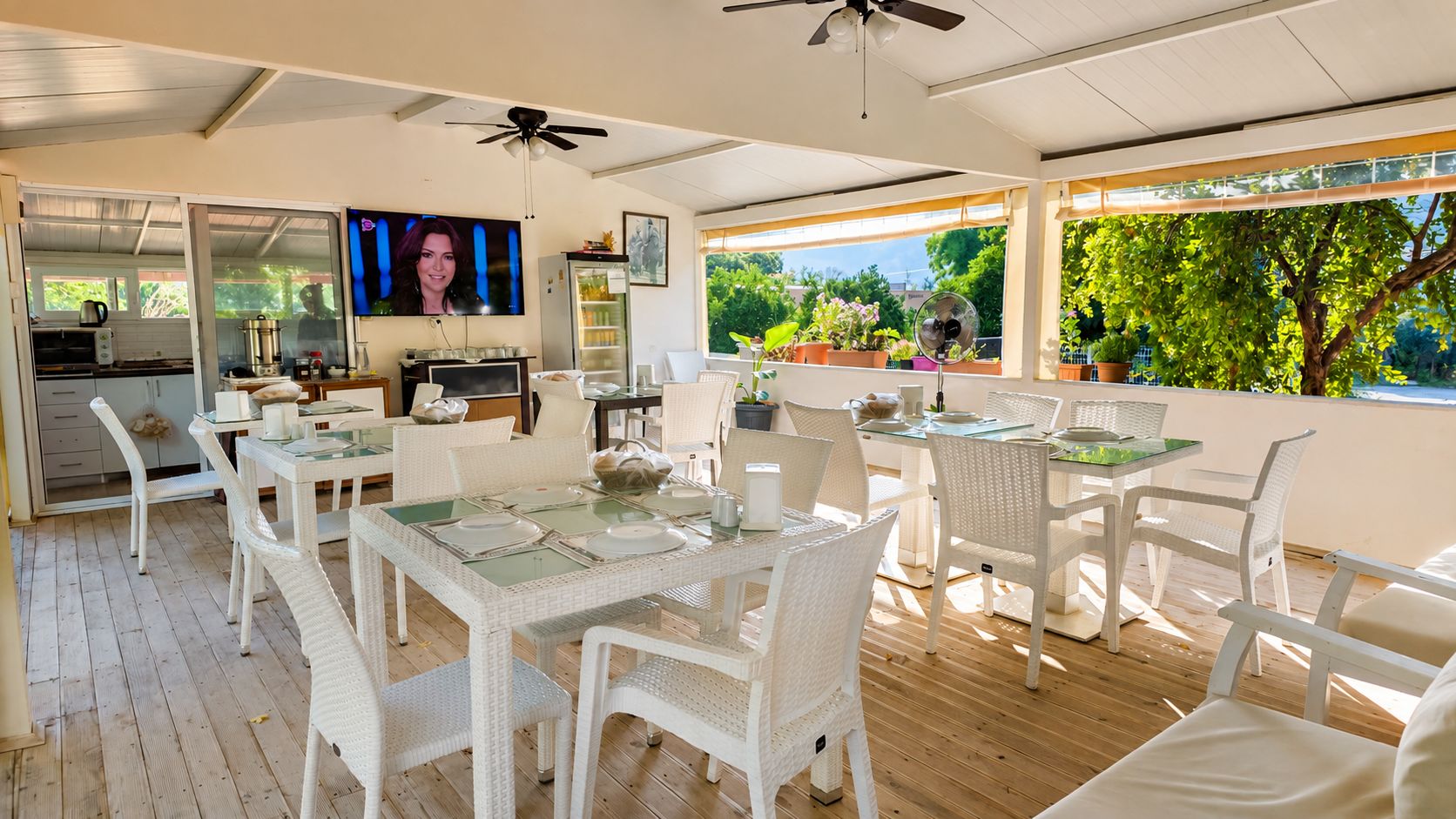 Un área de comedor al aire libre con mobiliario de mimbre blanco y una pantalla de televisión.