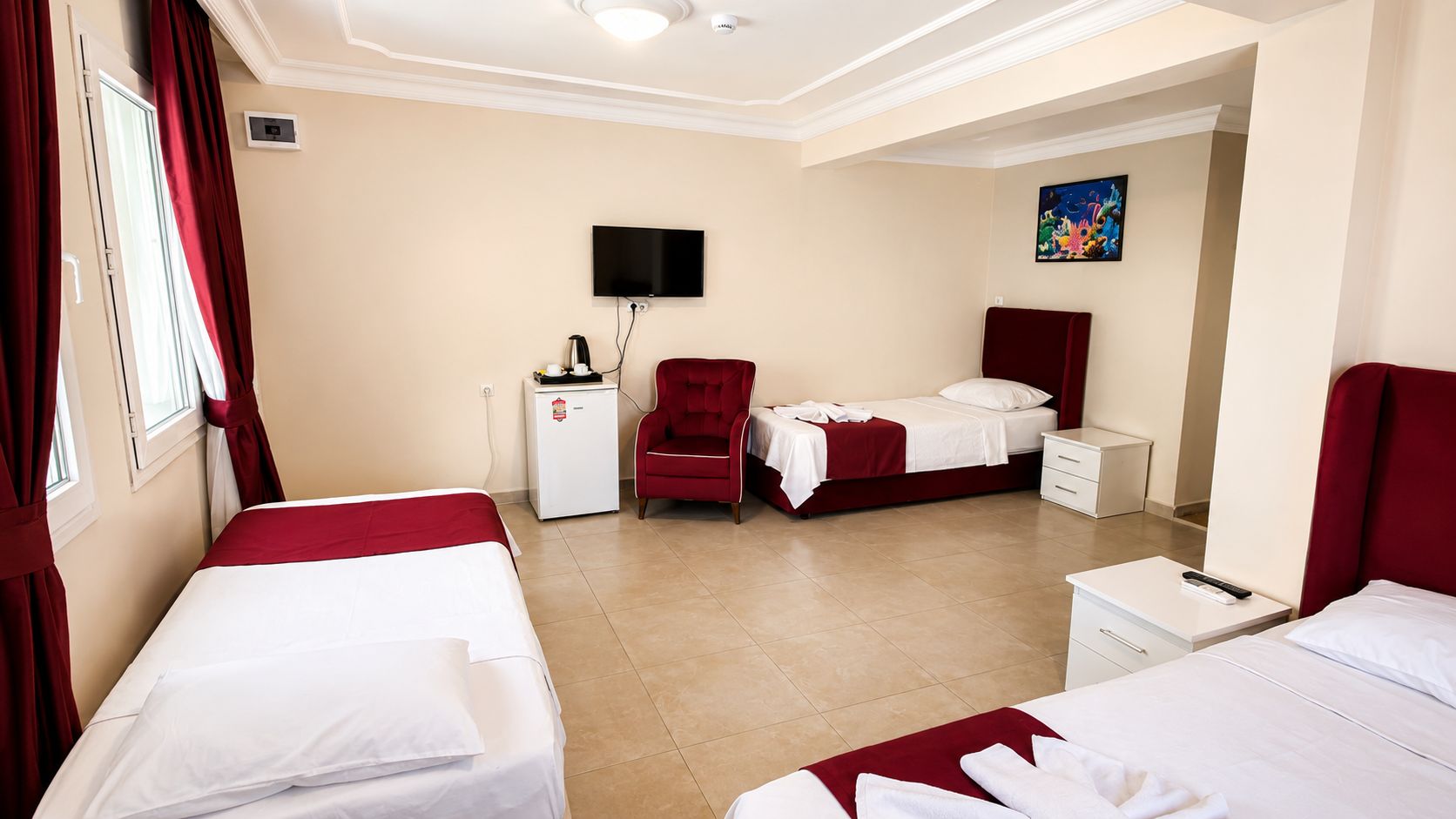 A hotel room with two beds, a desk, a chair, a television, and a small refrigerator.