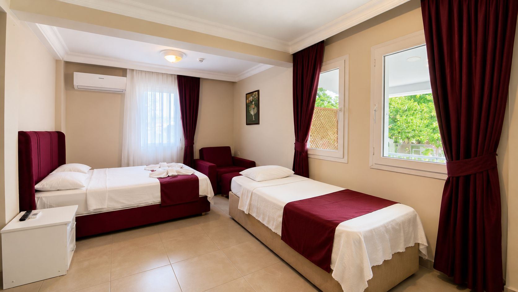 A hotel room with two beds, a desk, a chair, an air conditioning unit, and a window with curtains.