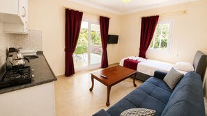 A compact living space with a kitchenette, a sofa, a bed, and a balcony with red curtains. - Bucak Apart Hotel Göcek (Fethiye)