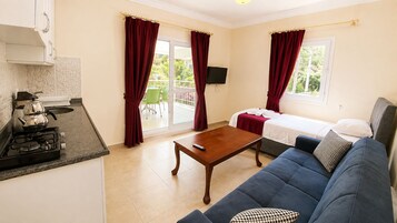 Un espacio habitable compacto con kitchenette, un sofá, una cama y un balcón con cortinas rojas.