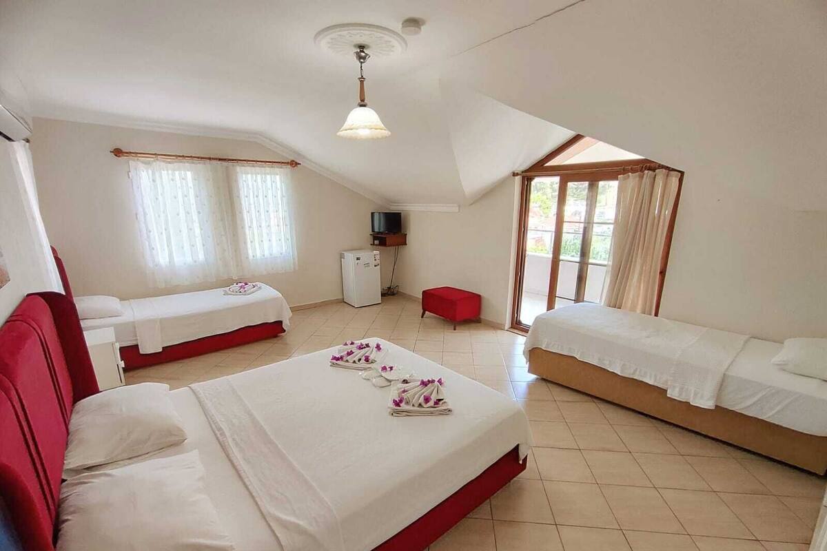 A hotel room with two single beds, a red sofa, a TV, a small fridge, and a window with curtains.