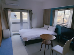 Une chambre d’hôtel avec un lit, une petite table ronde, une chaise, un téléviseur et une fenêtre avec des rideaux.