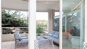 Un balcón con sofá y sillones, una mesita pequeña y una puerta de cristal que da a una habitación.