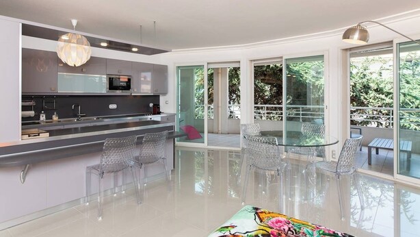 Una cocina moderna con una isla central, un comedor con mesas de vidrio y grandes puertas correderas que dan a un espacio exterior.