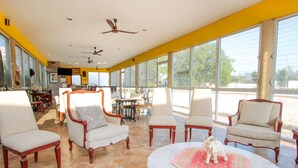 A spacious room with large windows, multiple chairs, a round table with a decorative rug, and ceiling fans. - Casa Bakab by Rotamundos (Mérida)