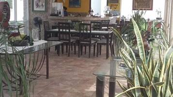 A spacious dining area with multiple tables and chairs, a tiled floor, and potted plants.