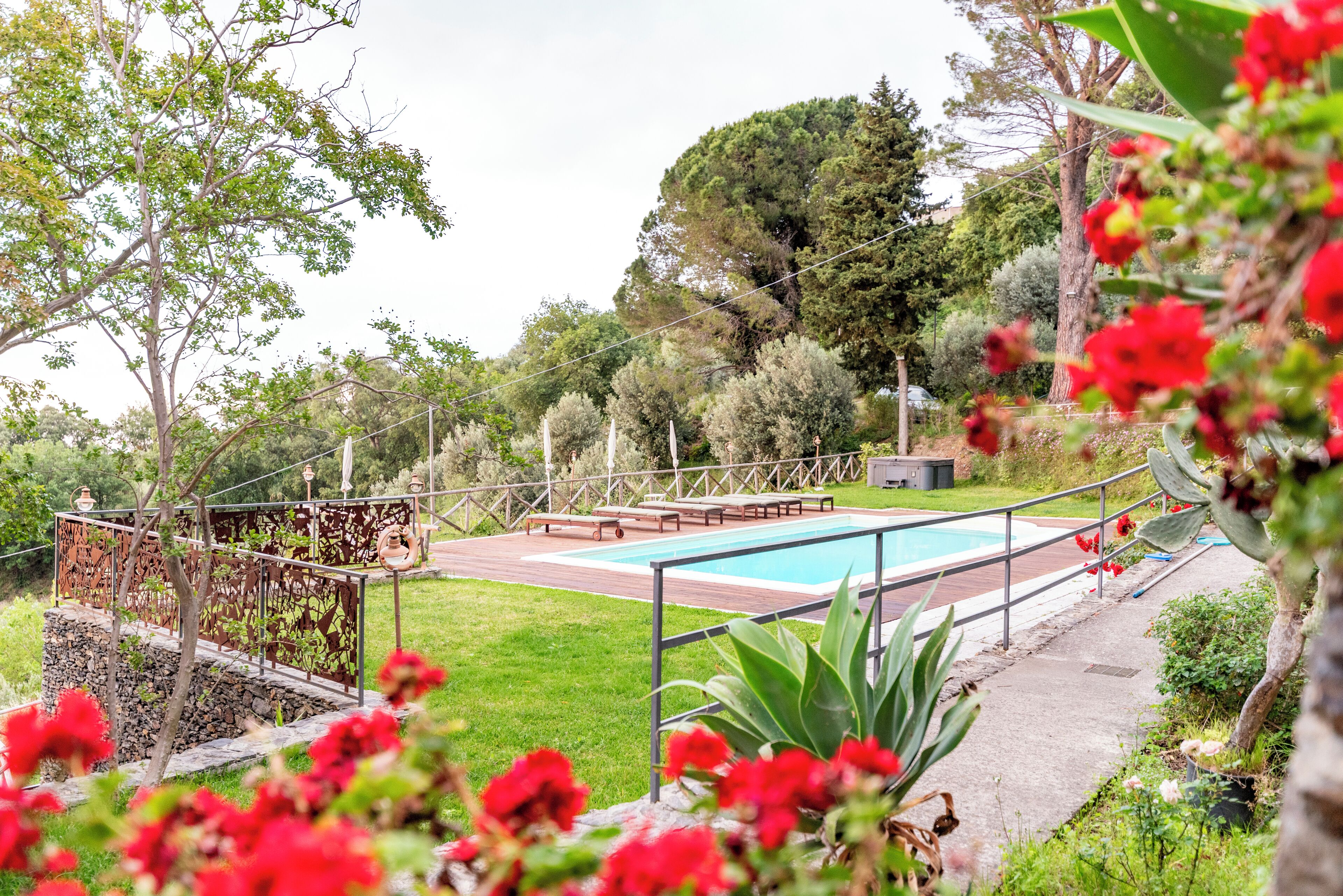 Una piscina amb un tram de fusta i barana metàl·lica, envoltada d'un jardí amb plantes i arbres diversos.