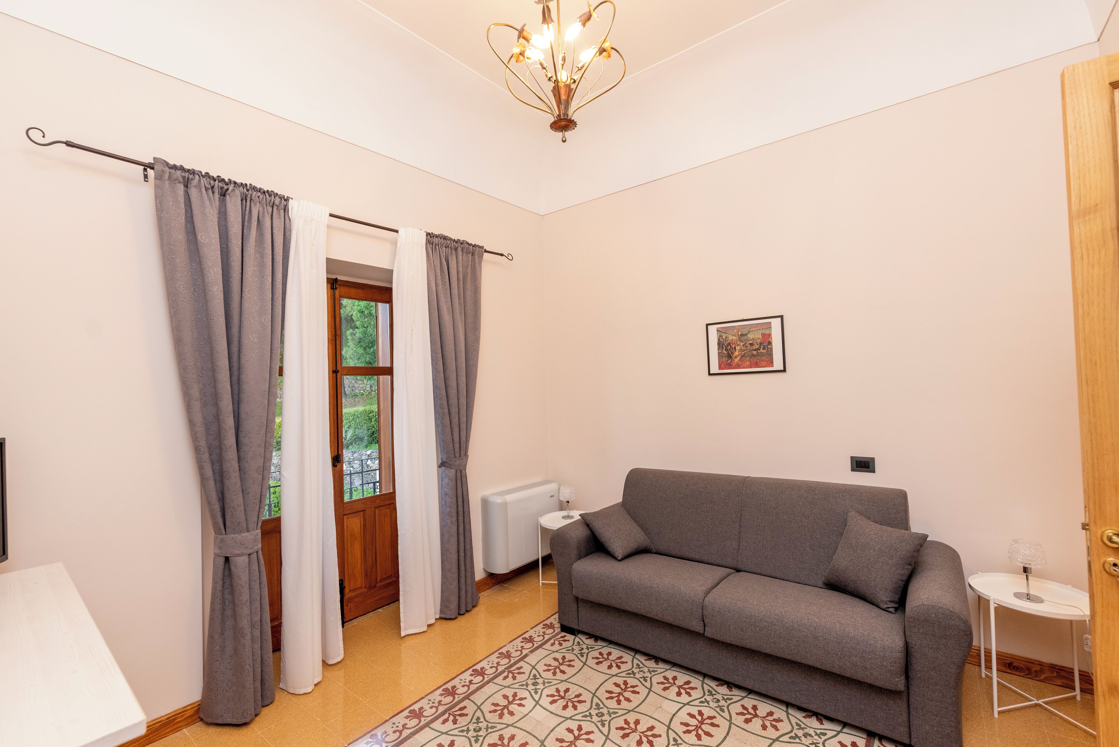 Una sala de estar con un sofá gris, un tapiz estampado, una mesita blanca pequeña y una araña.