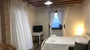 Quarto de hotel com uma cama, televisão, escrivaninha e vista para o mar.