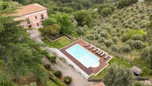 Vista aérea de uma propriedade com piscina, uma casa grande e vegetação ao redor.