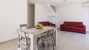 Een eethoek met een houten tafel en stoelen, een rode bank en een trap naar een hoger gelegen verdieping.