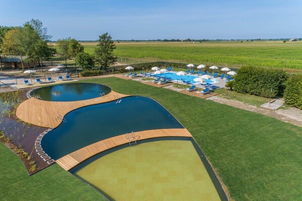 Una amplia piscina al aire libre con dos zonas diferenciadas, rodeada de césped con tumbonas y sombrillas.