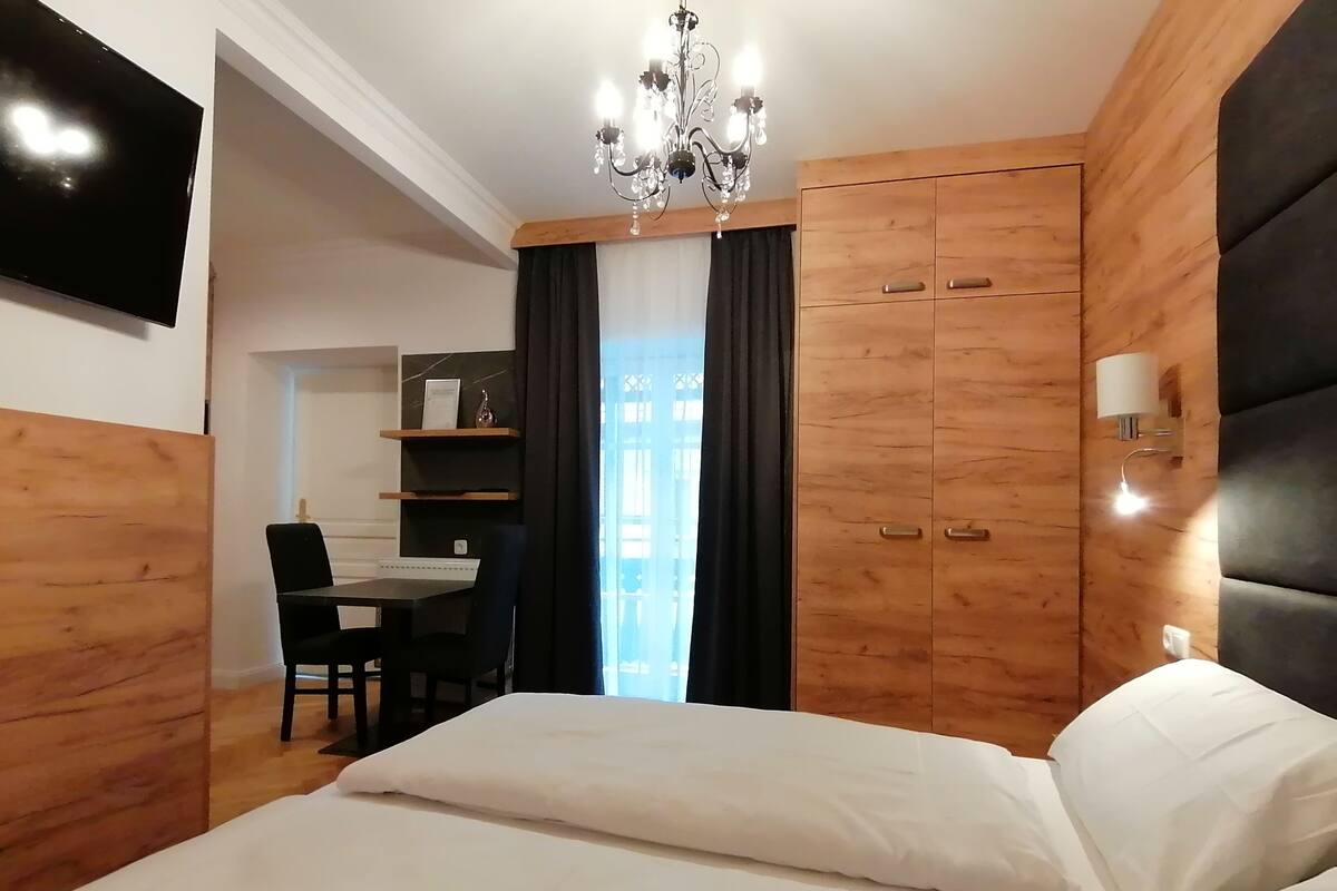 A bedroom with a bed, a desk, a chair, a chandelier, and wooden walls.