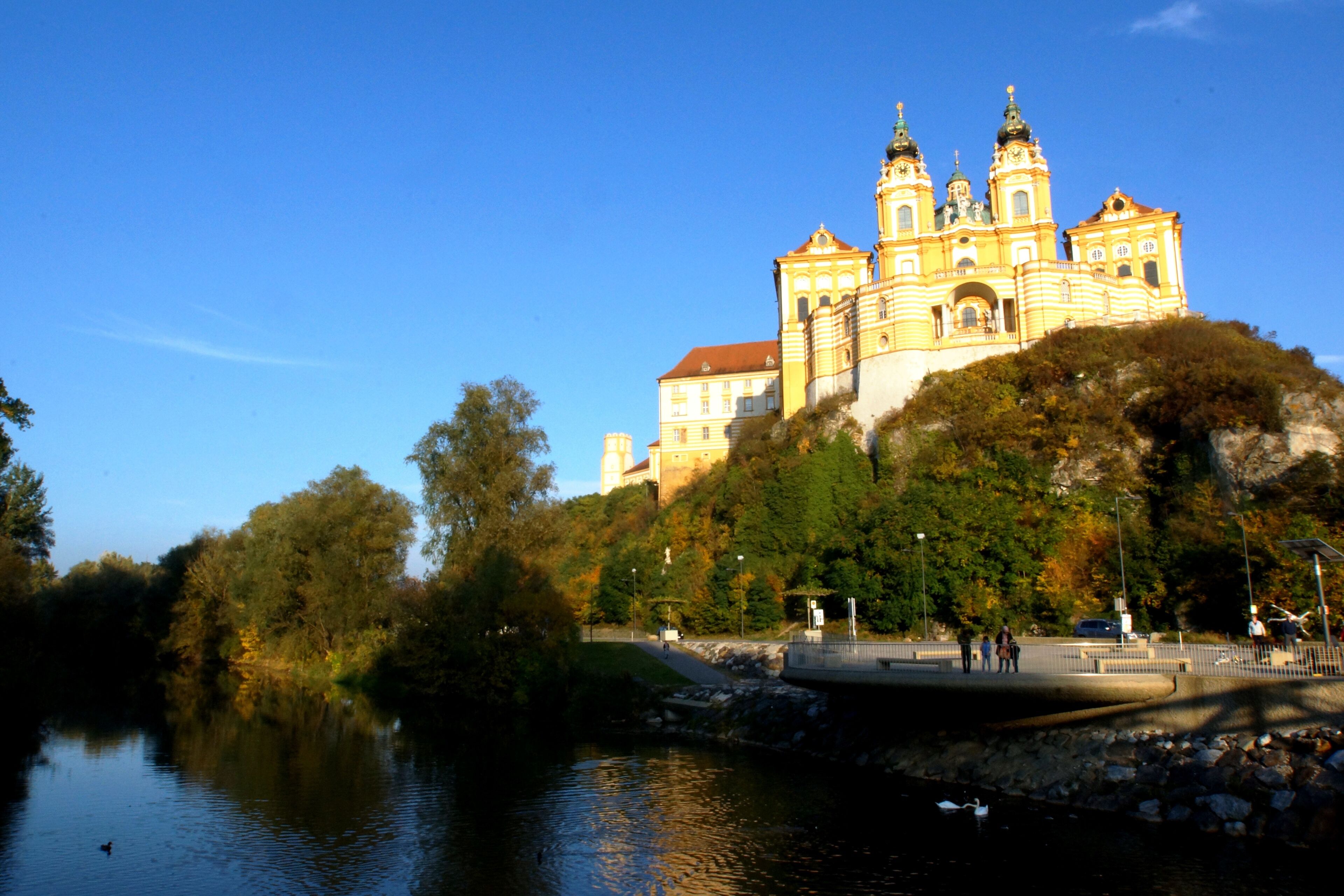 A historic building with multiple towers, situated on a hill overlooking a body of water.
