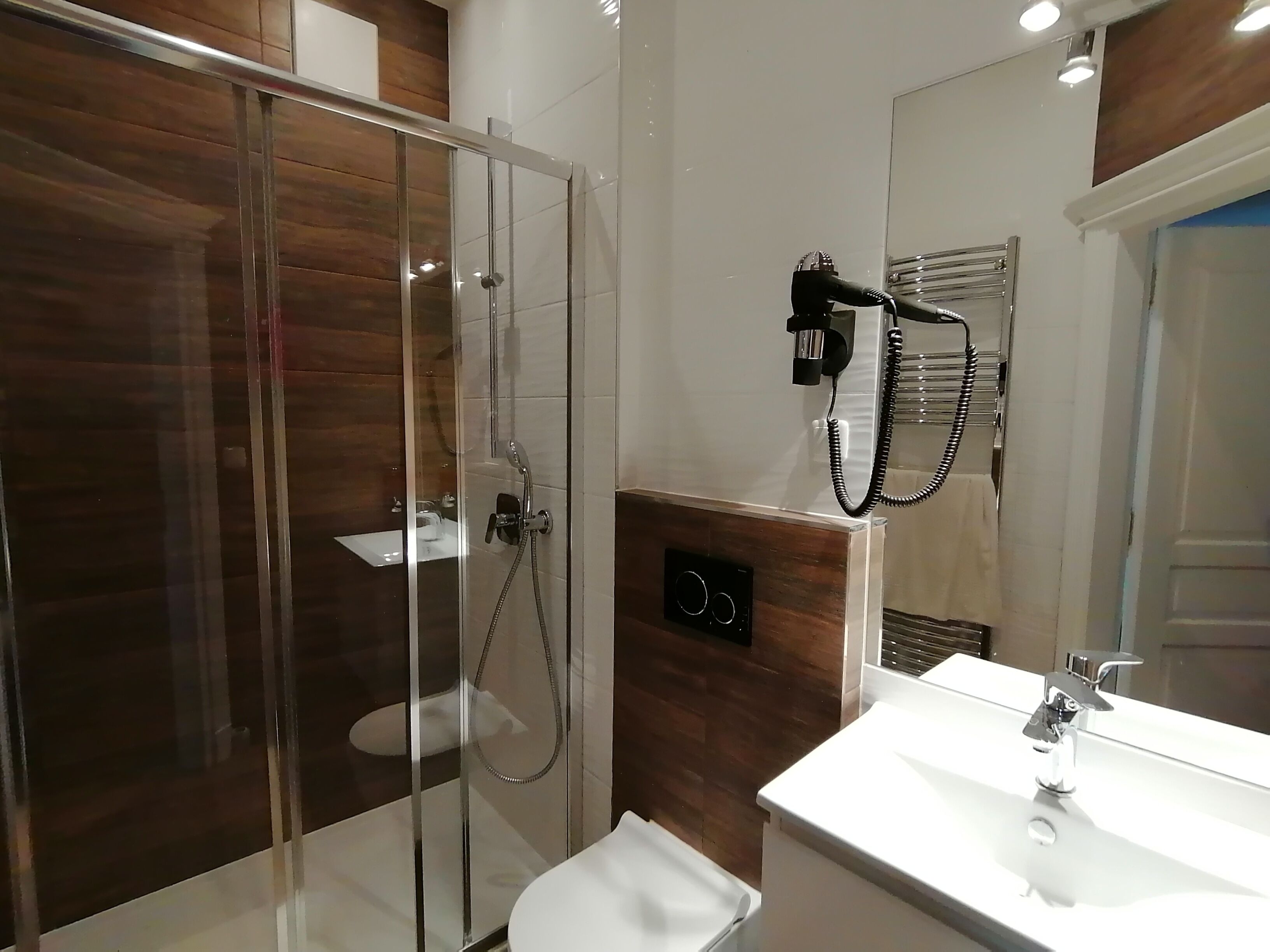 A modern bathroom with a glass-enclosed shower, a white sink, and a hairdryer mounted on the wall.