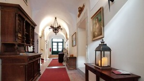 Um corredor com carpete vermelho, móveis de madeira, um lustre e um quadro na parede.