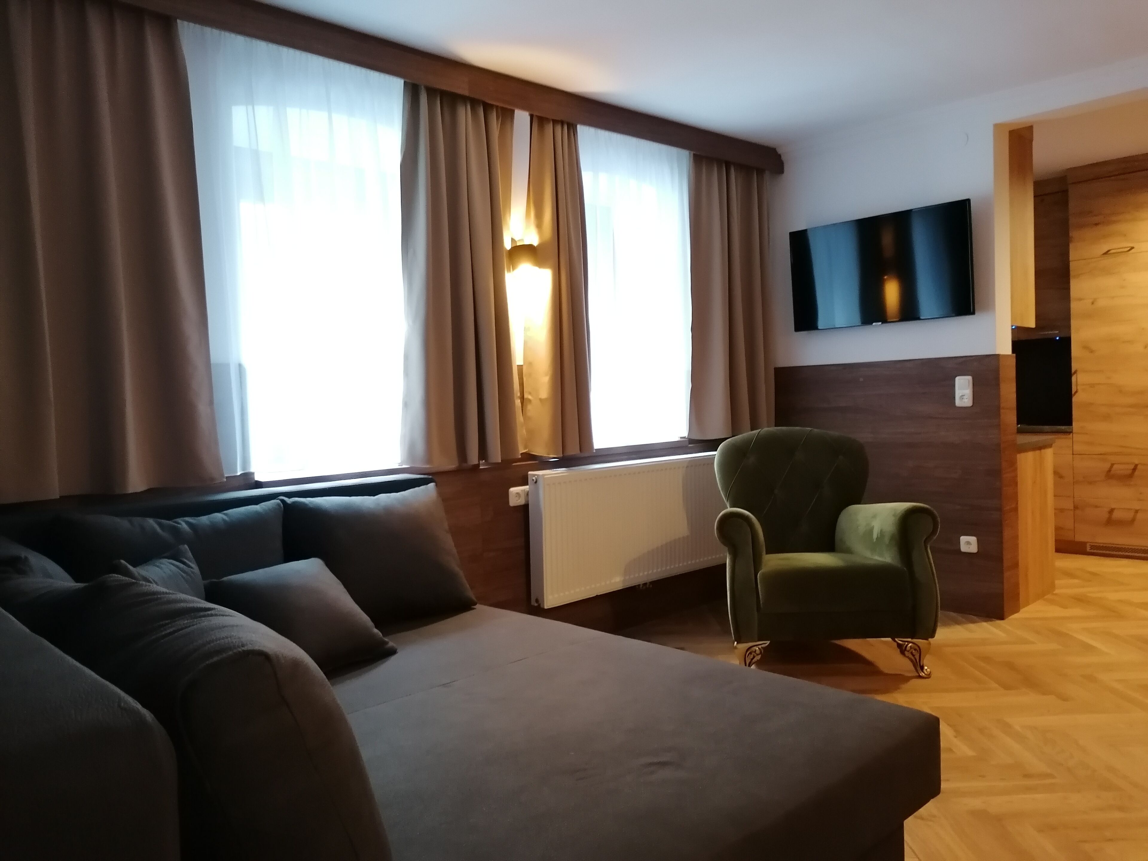 A modern living room with a sofa, a green armchair, a flat-screen TV, and a window with curtains.