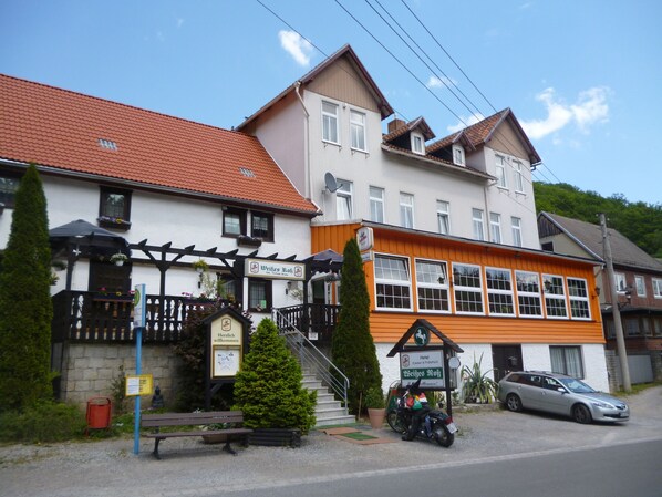 A two-story building with a sign indicating it is a hotel. There are stairs leading to the entrance, a bench outside, and a motorcycle parked in front. - Hotel Weißes Roß (Thale)