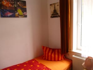 A small bedroom with a single bed, a red and yellow polka dot blanket, a striped pillow, and a painting of the Eiffel Tower on the wall. - Hotel Weißes Roß (Thale)