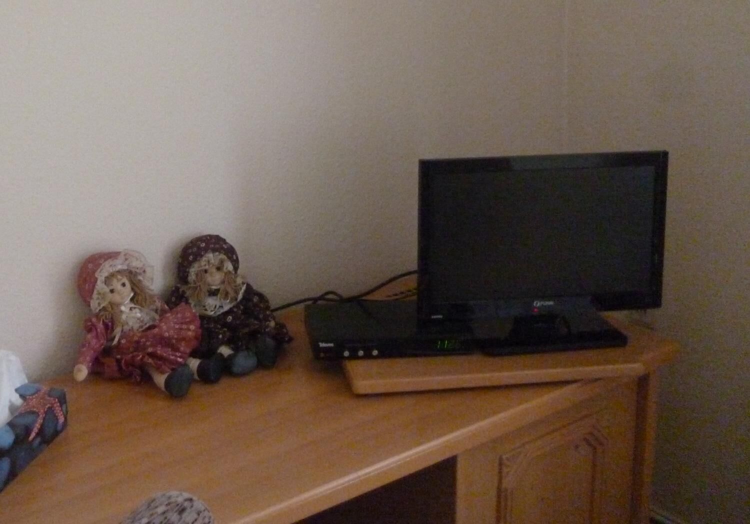 A wooden desk with a television, two dolls, and a starfish decoration.