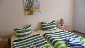 Uma cama de casal com roupa de cama listrada em verde e branco, uma mesa de cabeceira com abajur e um quadro de bambu na parede.