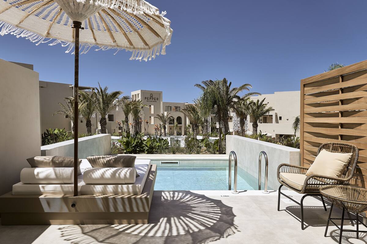 A poolside area with lounge chairs, a large umbrella, and a view of the resort buildings in the background.