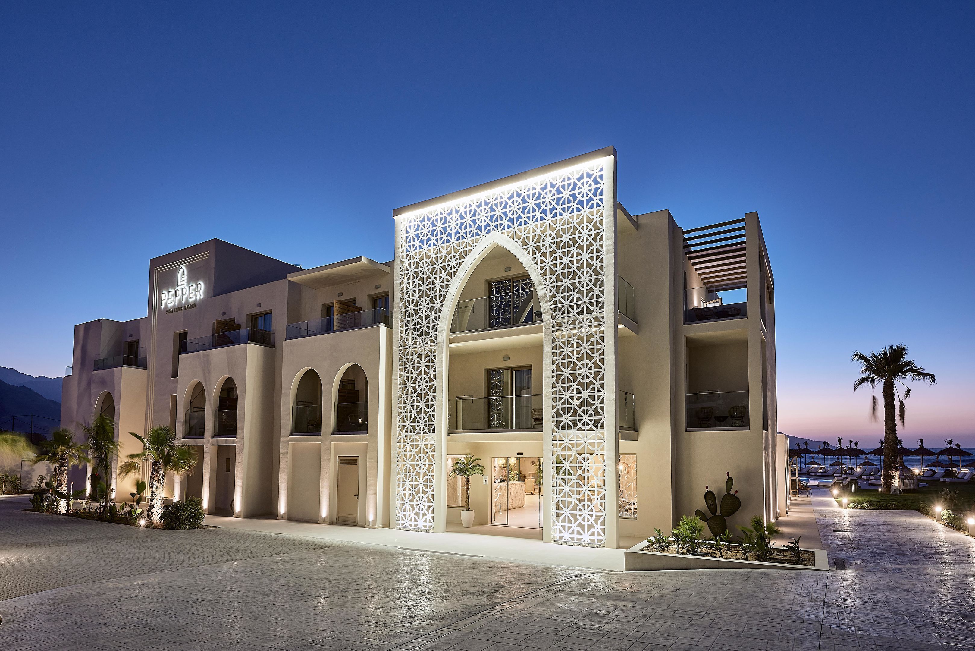 Un hôtel moderne doté d’une entrée arquée imposante, d’une enseigne bien visible et d’un balcon donnant sur un espace paysager aménagé.