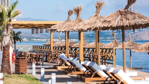 A beachside lounge area with wooden loungers and thatched umbrellas, overlooking the sea.