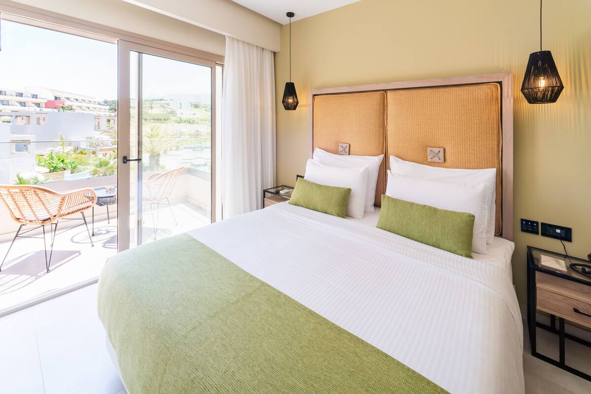 A hotel room with a large bed, a balcony with a chair, and a view of buildings.