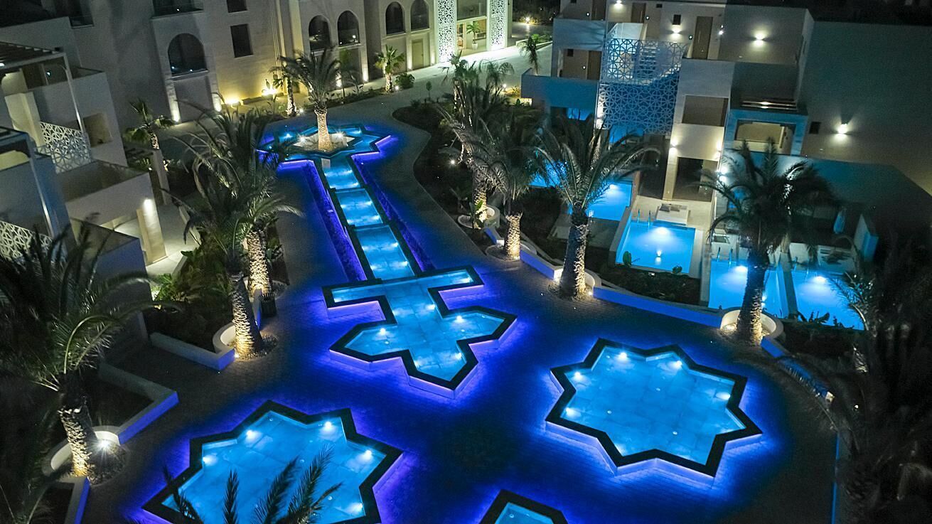 A hotel courtyard with a pool, palm trees, and illuminated star-shaped patterns on the ground.