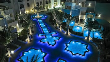 A hotel courtyard with a pool, palm trees, and illuminated star-shaped patterns on the ground.