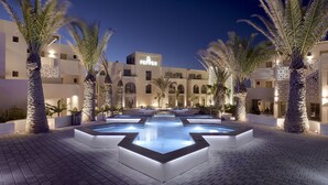 A hotel courtyard with a swimming pool, palm trees, and a building with a 'PEPPER' sign.